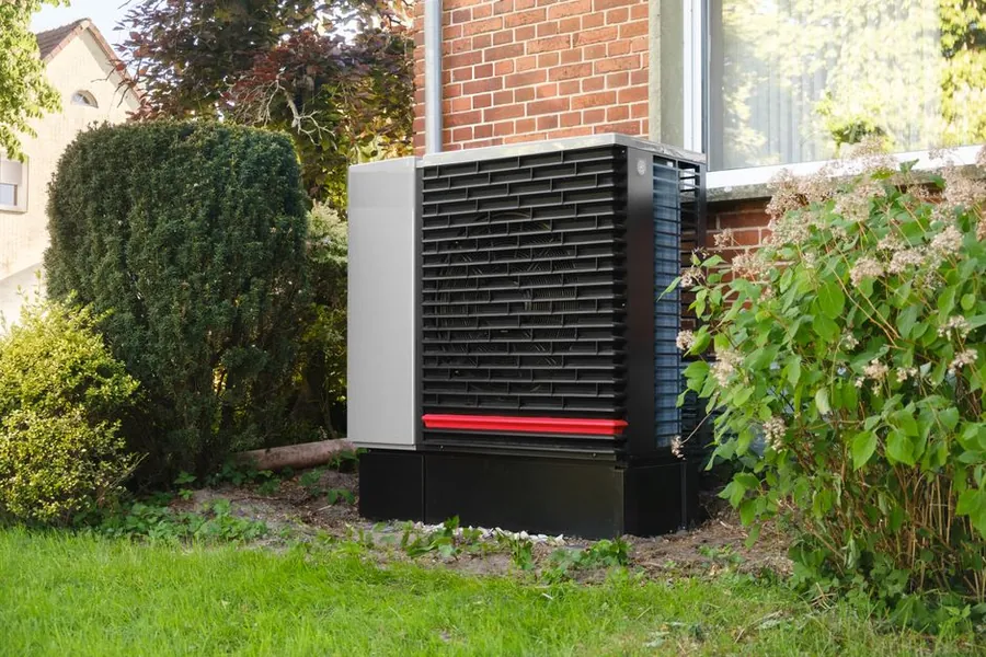 An air source heat pump standing in the garden of a brick house